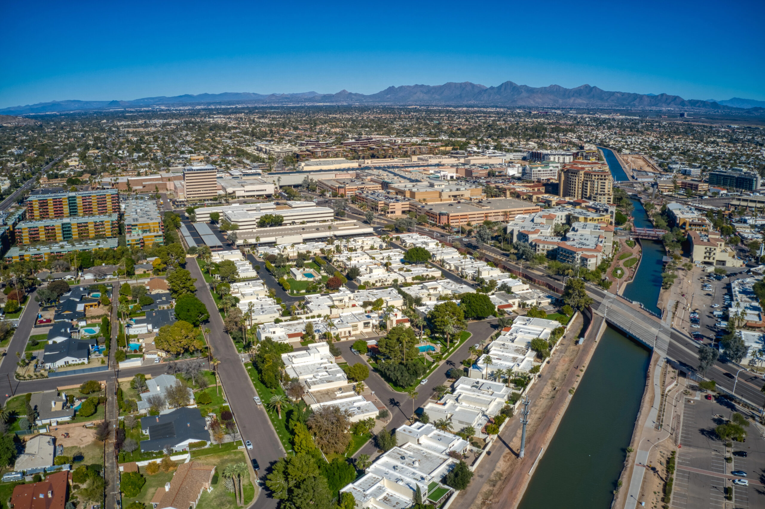 Scottsdale Aerial view of Scottsdale, AZ, showcasing residential and commercial areas, including white-roofed houses, green spaces, and a canal, highlighting the city's landscape and urban development.