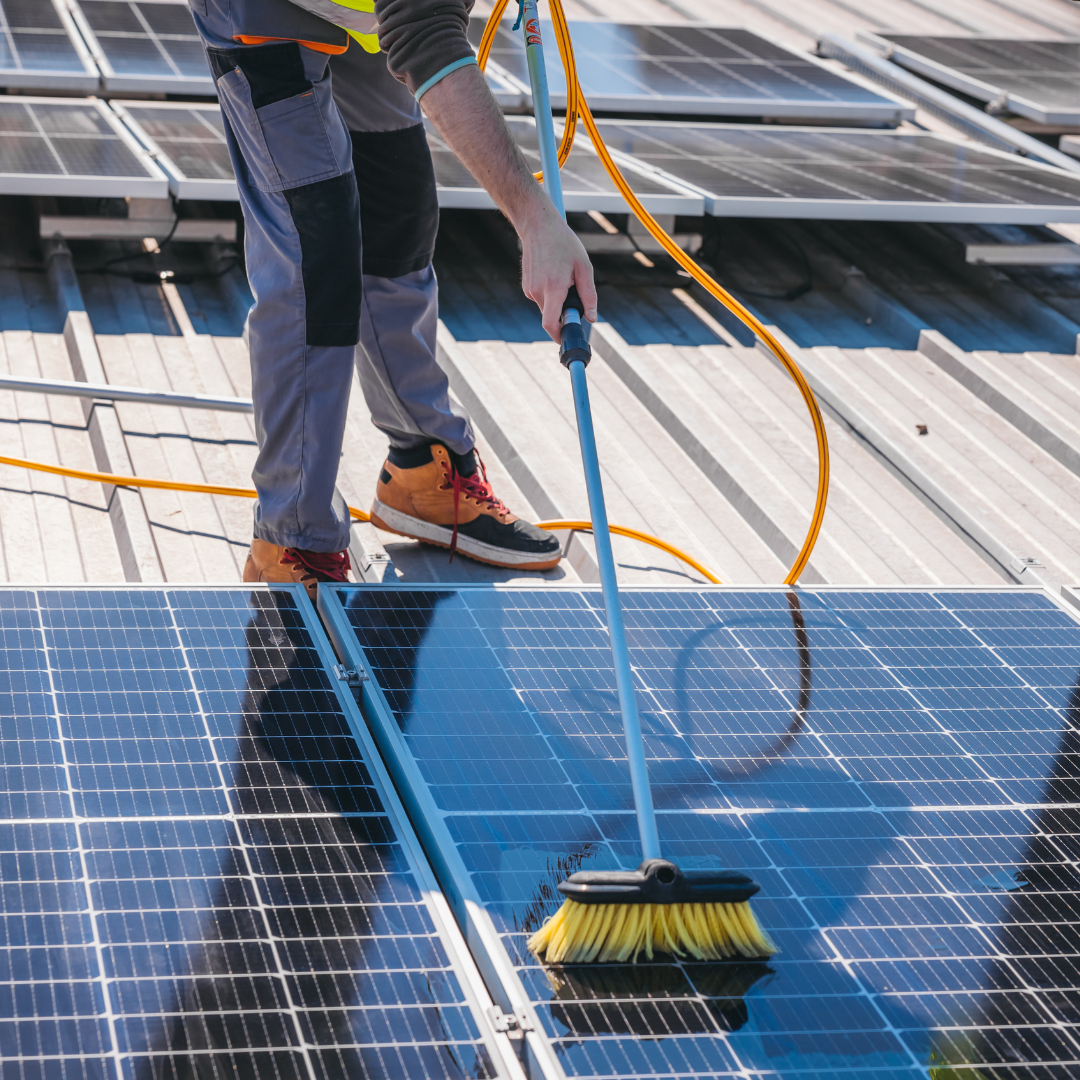 Worker cleaning solar panels on a rooftop using a brush and water hose, emphasizing solar panel maintenance for efficiency in Scottsdale.