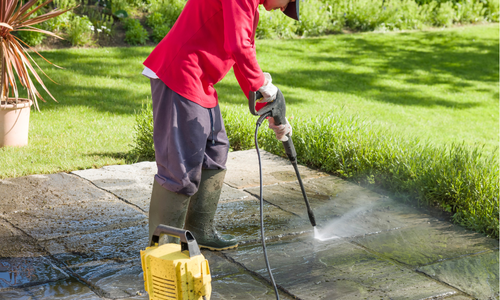 Person using a pressure washer on a stone patio, demonstrating professional cleaning services for residential properties in Arizona's climate.