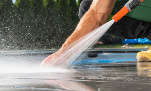 Person using a pressure washer to clean a patio surface, showcasing residential cleaning services by Power Crew Pressure Washing.
