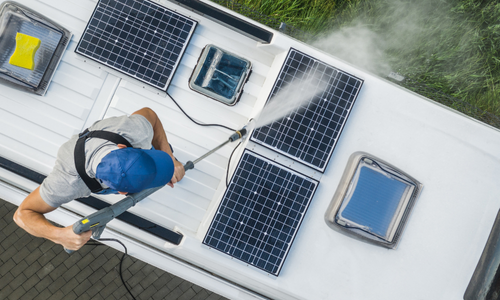 Person using a pressure washer to clean solar panels on a roof, emphasizing energy efficiency and maintenance for Arizona properties.