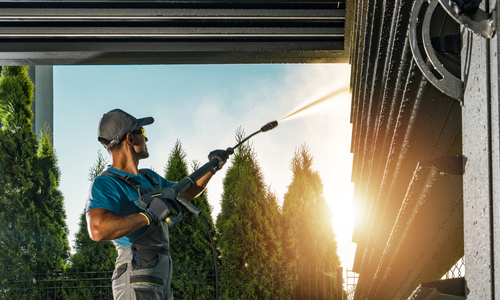 Professional pressure washing service in action, technician using high-pressure washer to clean exterior surfaces, surrounded by greenery, showcasing the effectiveness of cleaning solutions for residential and commercial properties in Arizona.