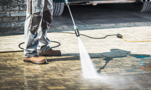 Person using a pressure washer on a paver driveway, showcasing professional cleaning service for residential properties in Scottsdale, AZ.