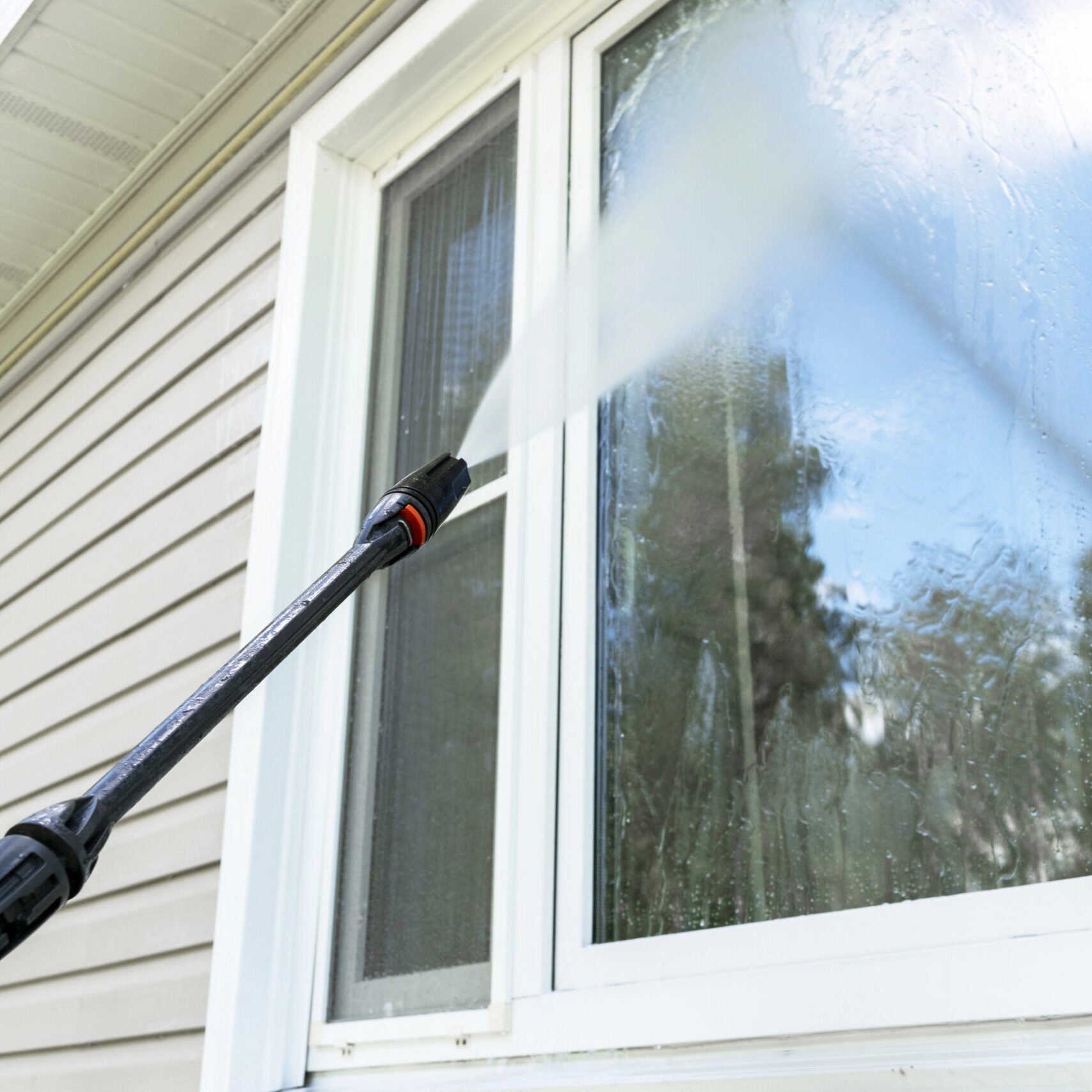 Window Benefits Professional window cleaning in Scottsdale, with a pressure washer spraying water on a glass window, showcasing the cleaning process to enhance clarity and curb appeal.