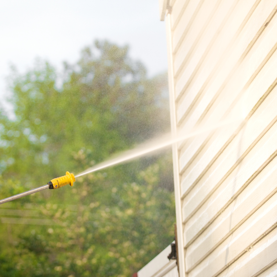 Pressure washing a home’s exterior with a spray nozzle, removing dirt and mildew from siding in a residential setting.